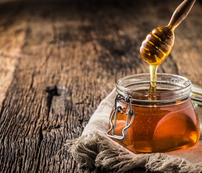 Honey jar with dipper on old woodn table.